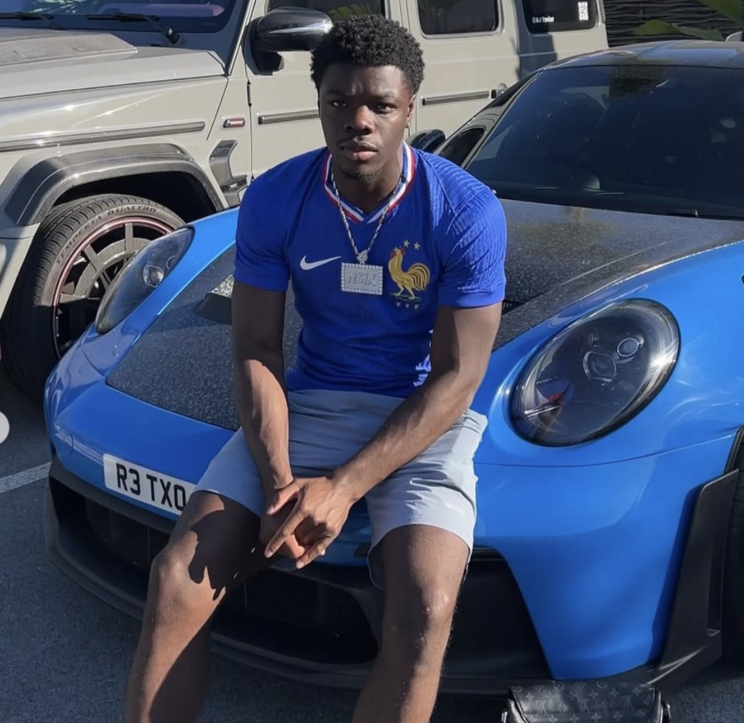 Nsix sitting on the front of a blue Porsche wearing a France football shirt